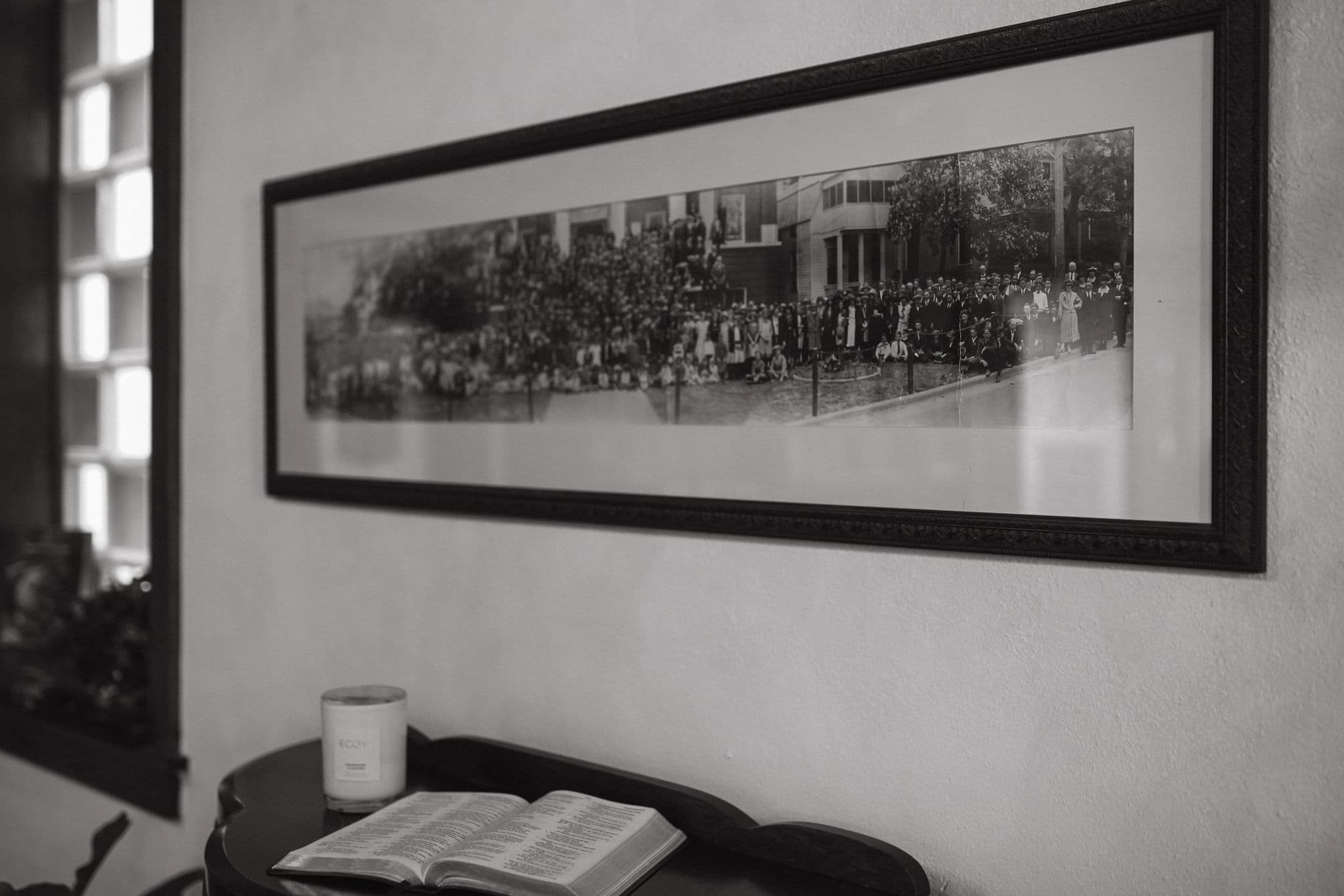 Historic black and white panoramic photograph framed on a wall above an open Bible and candle in a serene room.