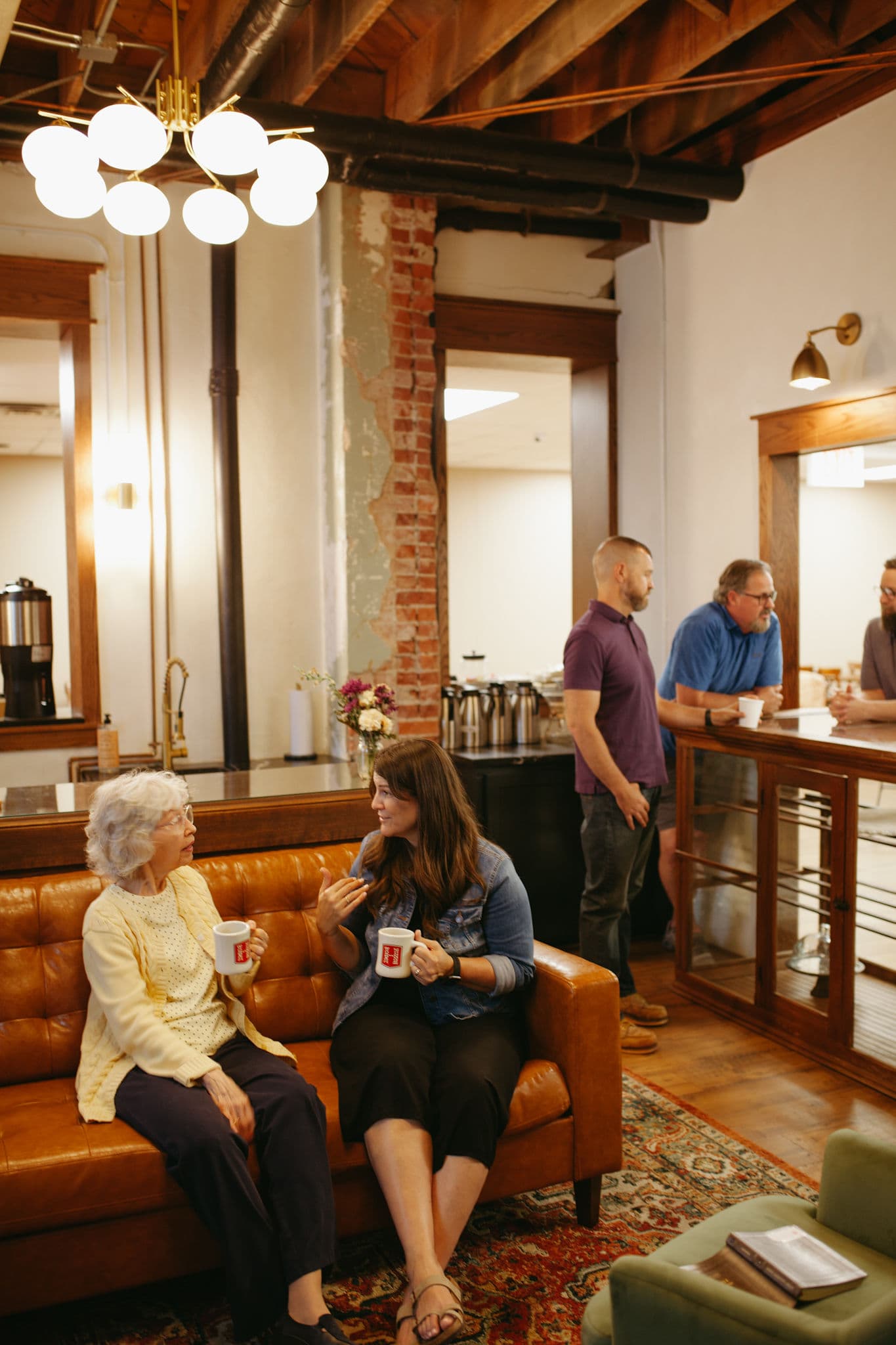 Two women from different generations sharing a heartfelt conversation while enjoying coffee on a comfortable leather couch in a welcoming community space.