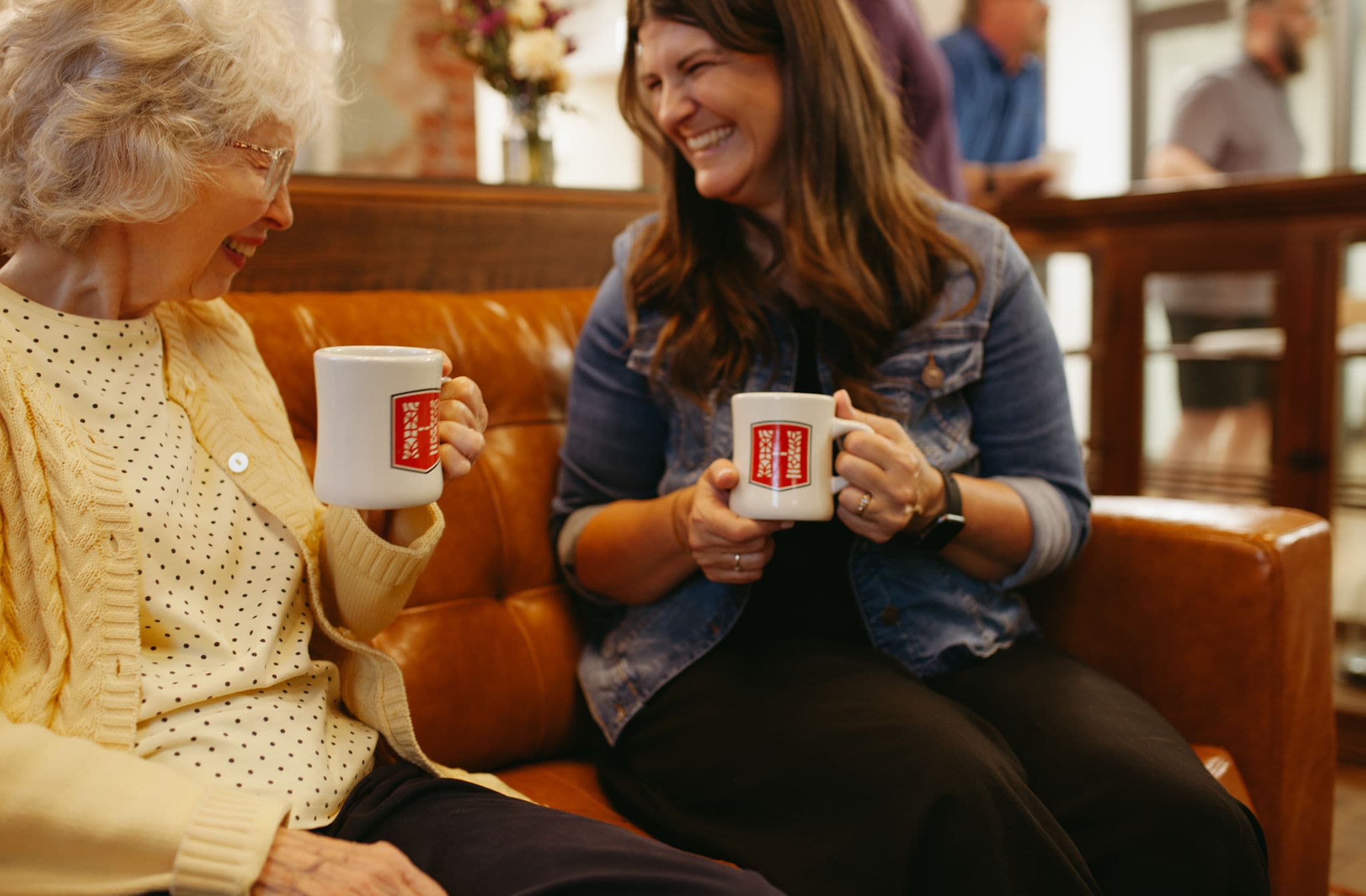Two women from different generations sharing a heartfelt conversation while enjoying coffee on a comfortable leather couch in a welcoming community space.